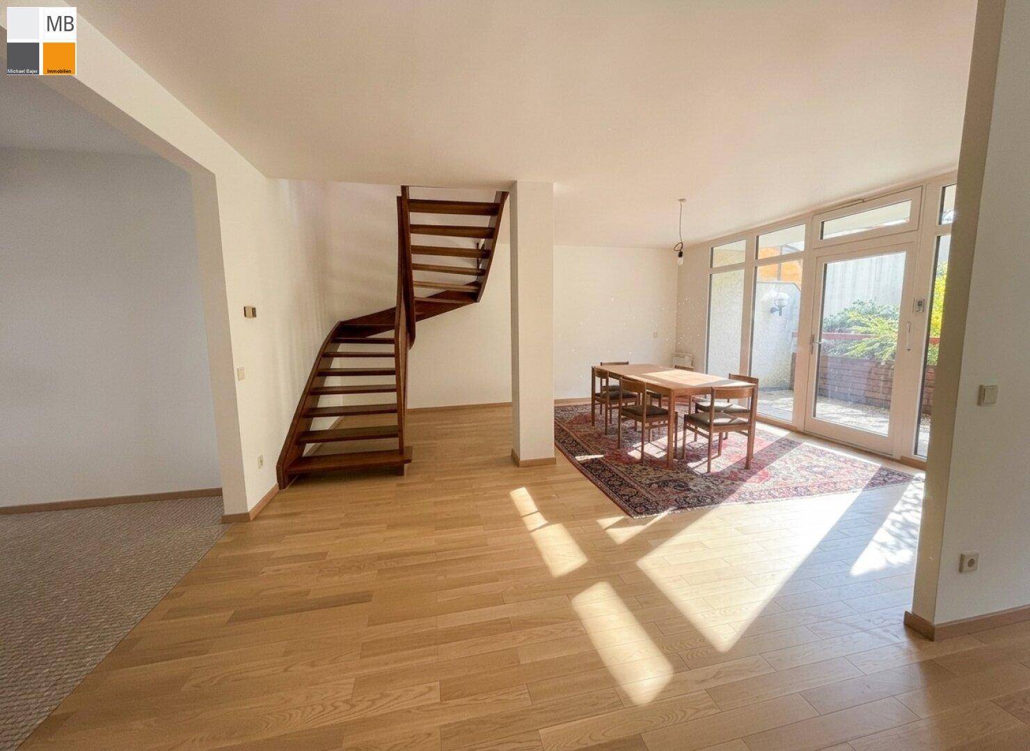 Lichtdurchfluteter Wohnbereich mit Parkettboden, Wendeltreppe und Zugang zu einem Außenbereich.