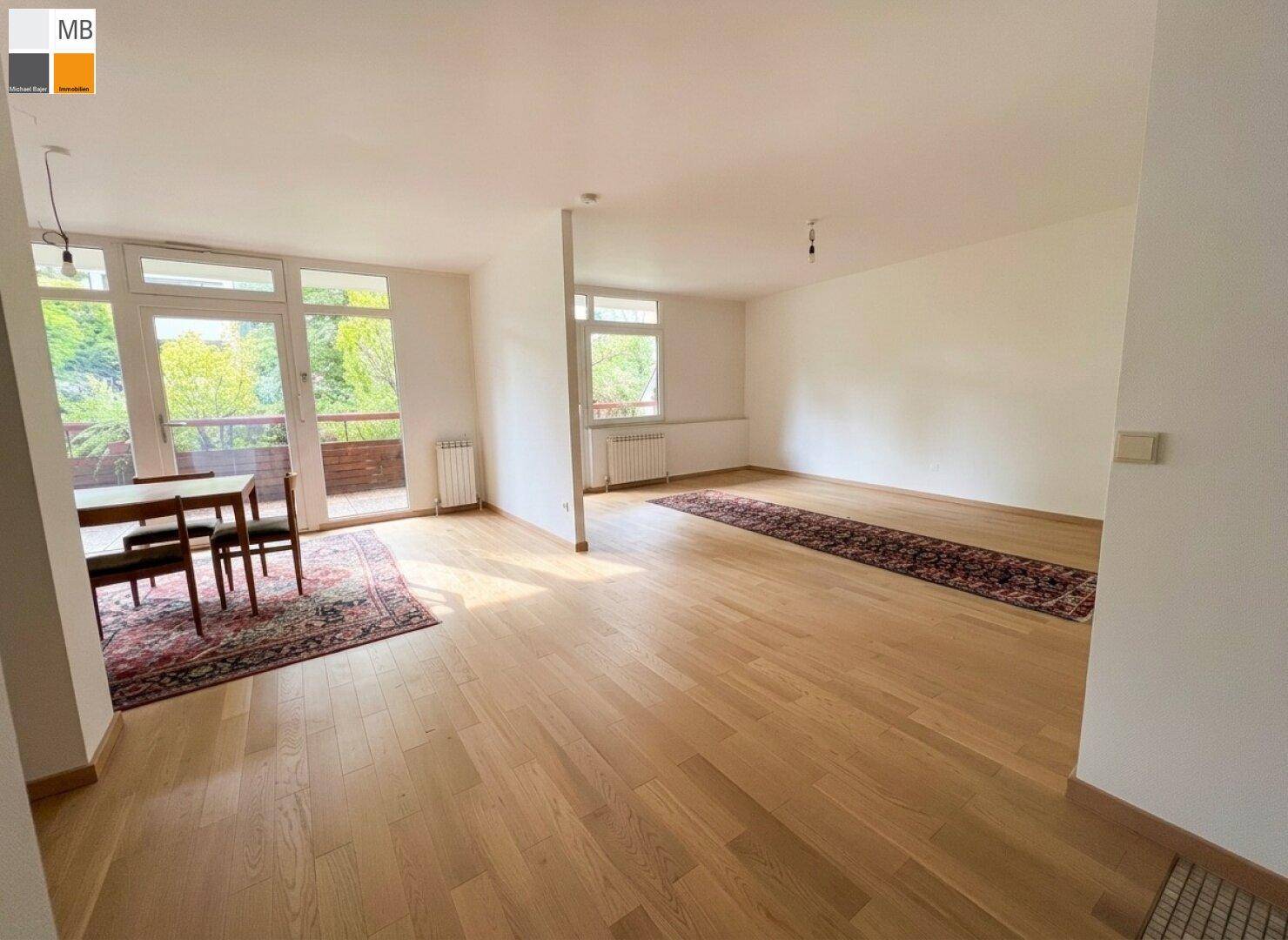Heller Wohn- und Essbereich mit Parkettboden, großen Fenstern und Blick ins Grüne.