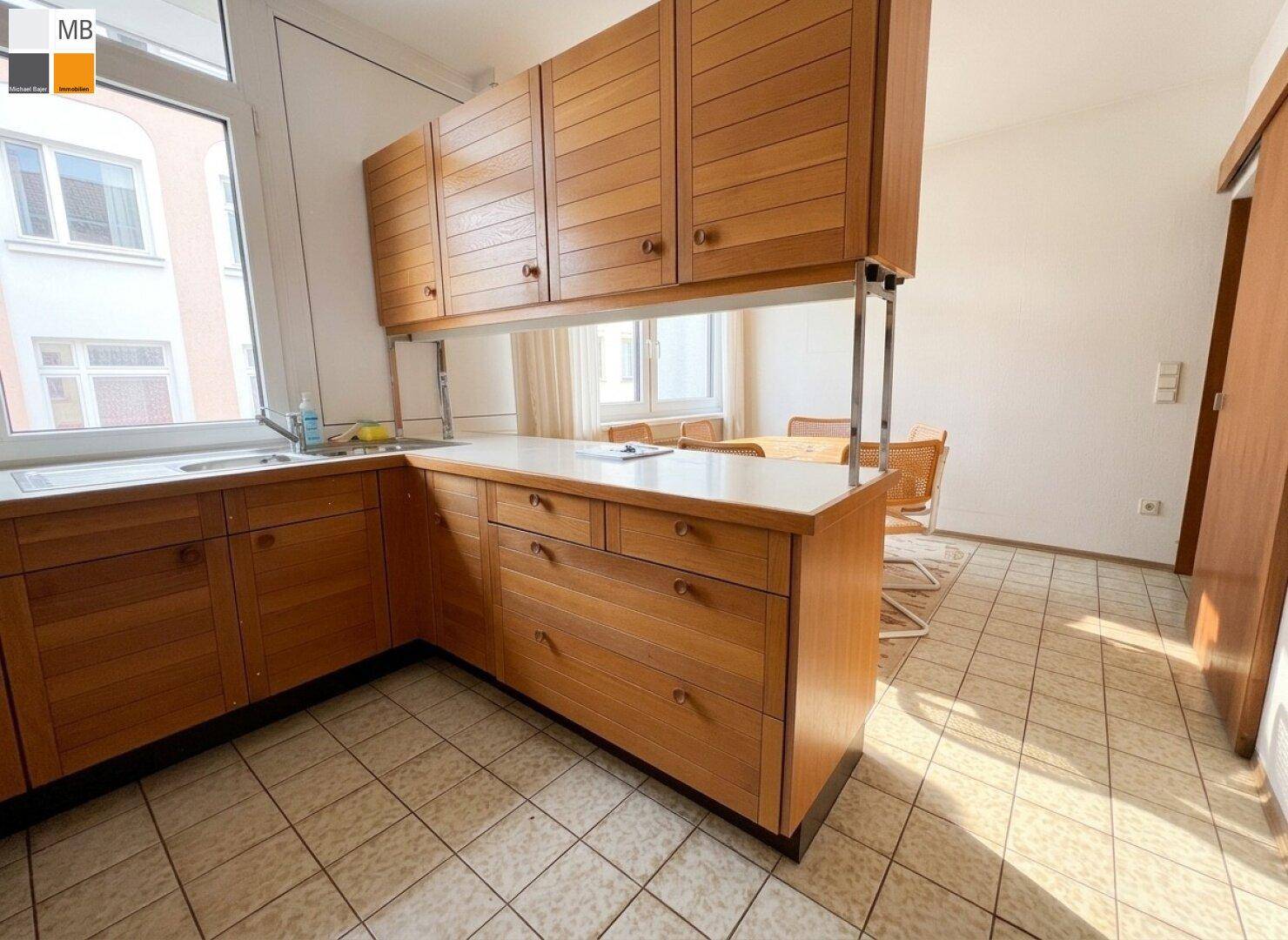 Funktionale Küche mit Holzschränken, Fliesenboden und Blick auf den Essbereich.
