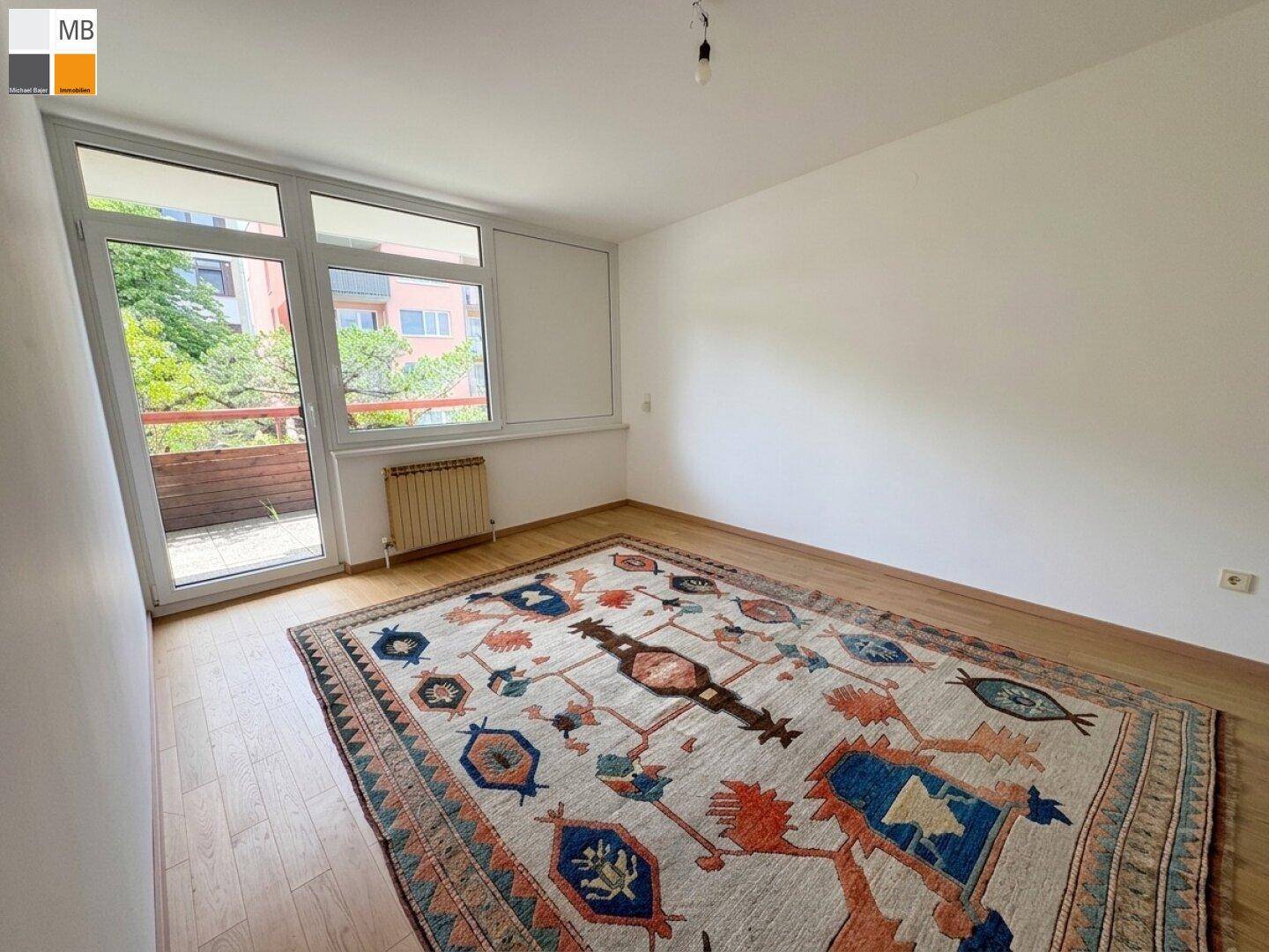 Helles Schlafzimmer mit Parkettboden, großem Fenster und Zugang zum Balkon.
