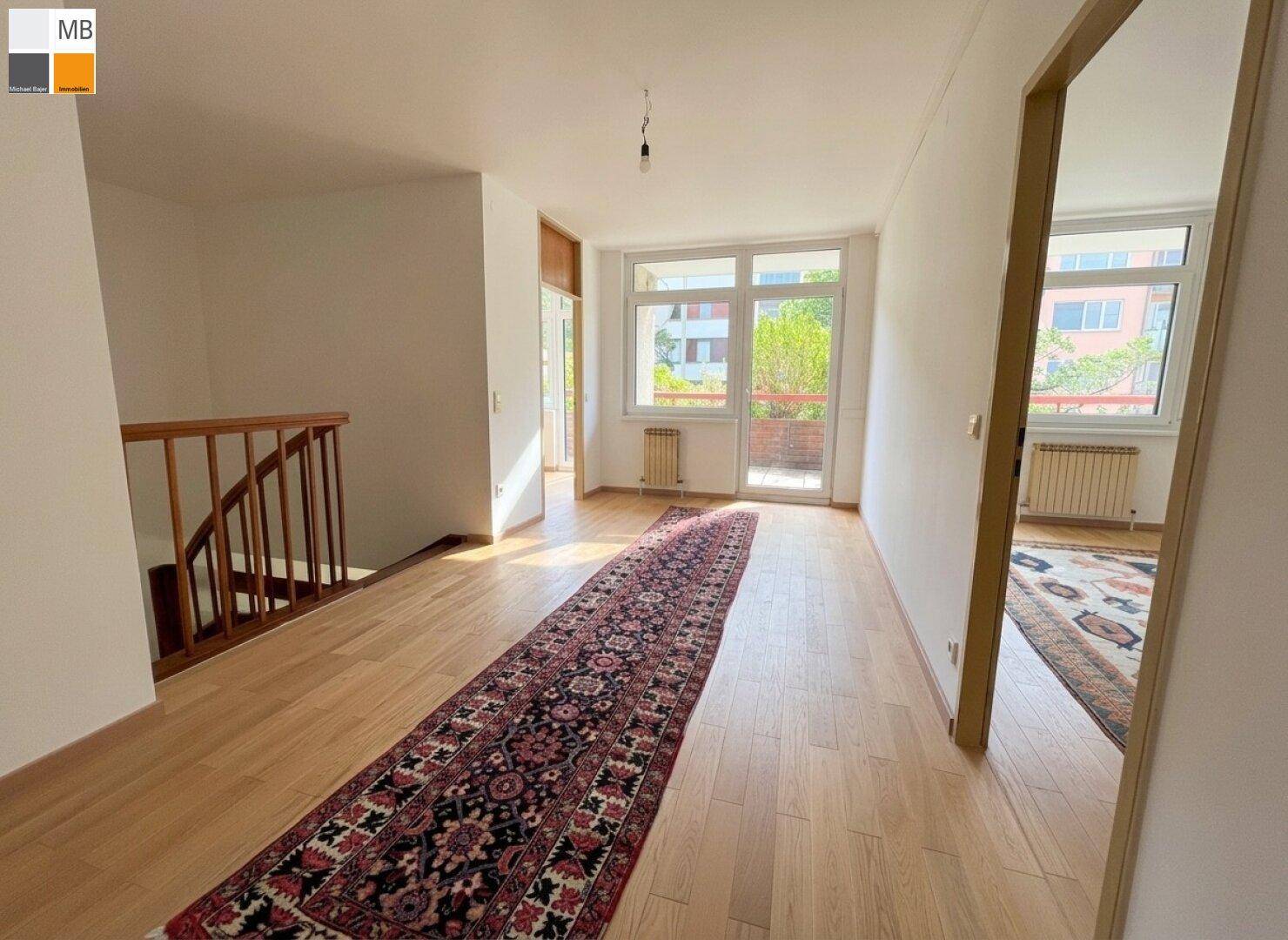 Geräumiger Flur mit Parkettboden, Holztreppe und viel natürlichem Licht.