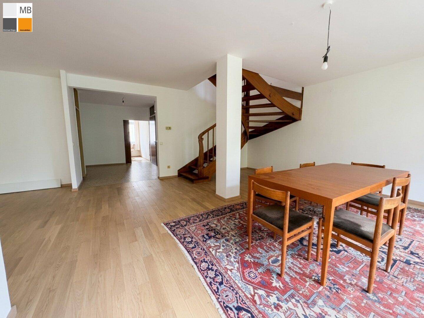 Offener Wohnbereich mit Esstisch, Parkettboden und eleganter Holztreppe zum Obergeschoss.