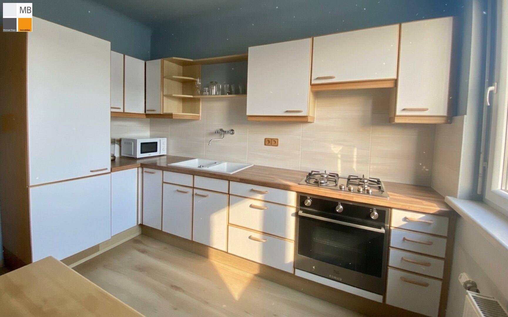 Funktionale Küche mit weißen Schränken, Holzarbeitsplatte und Gasherd, gut beleuchtet durch das Fenster.
