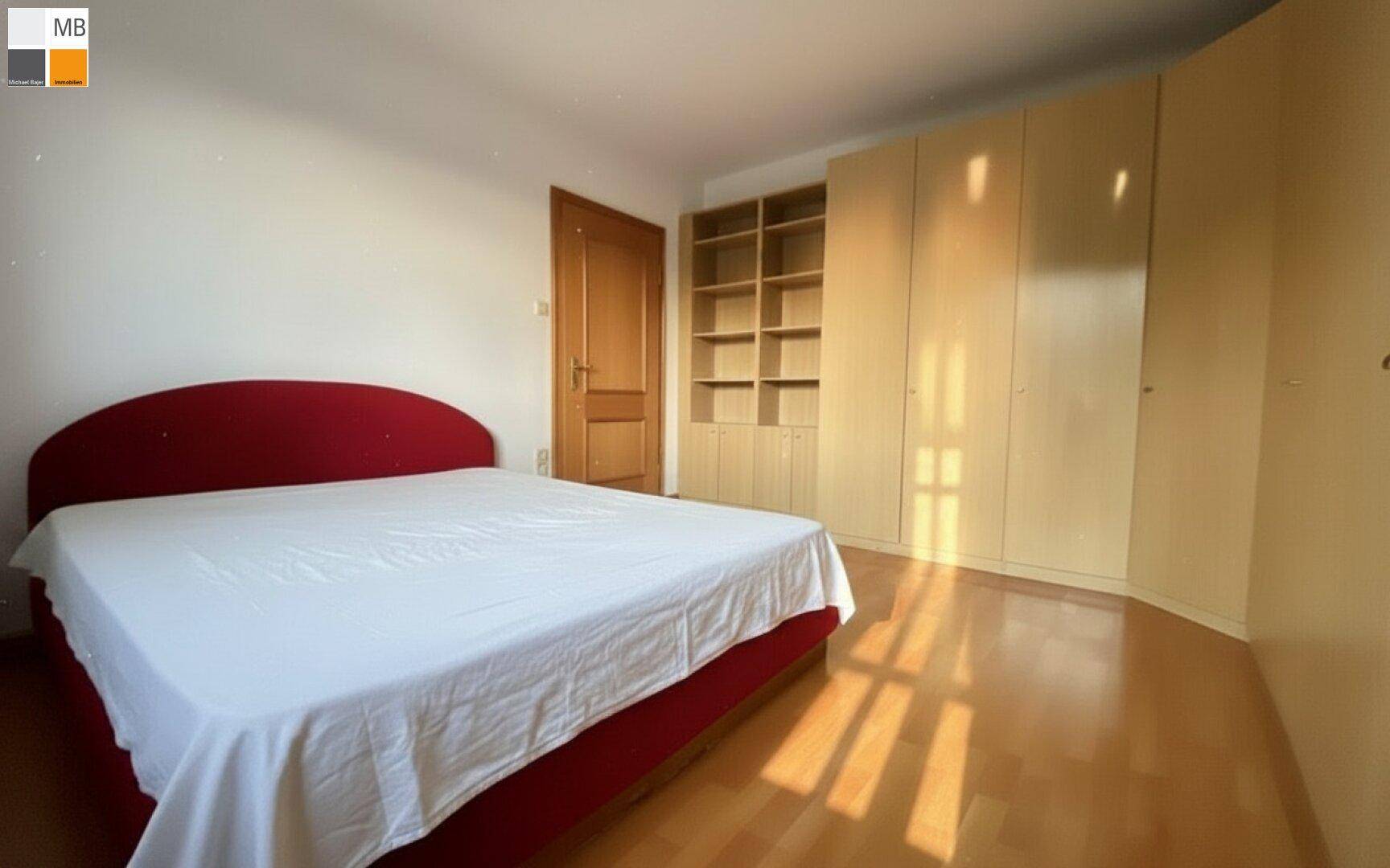 Geräumiges Schlafzimmer mit Holzboden, rotem Bett und Einbauschränken, hell und funktional.