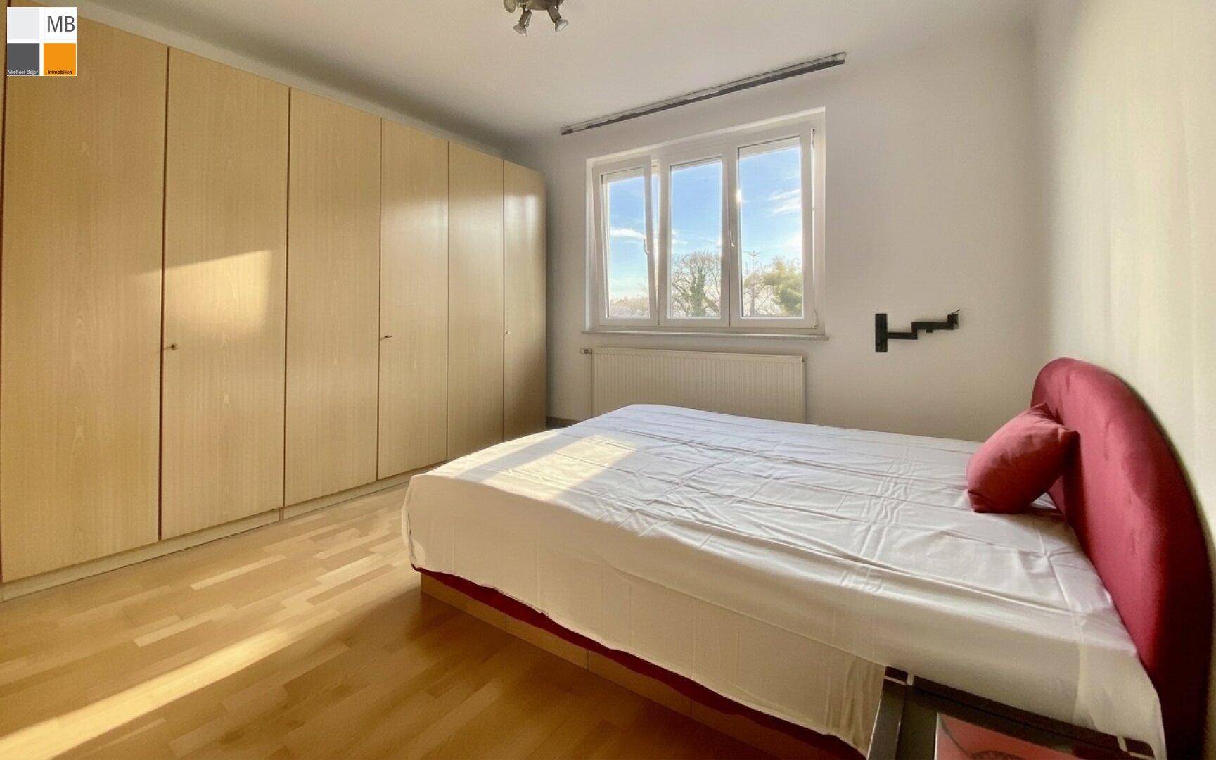 Helles Schlafzimmer mit großem Fenster, Holzboden und Einbauschränken, bietet viel Stauraum.