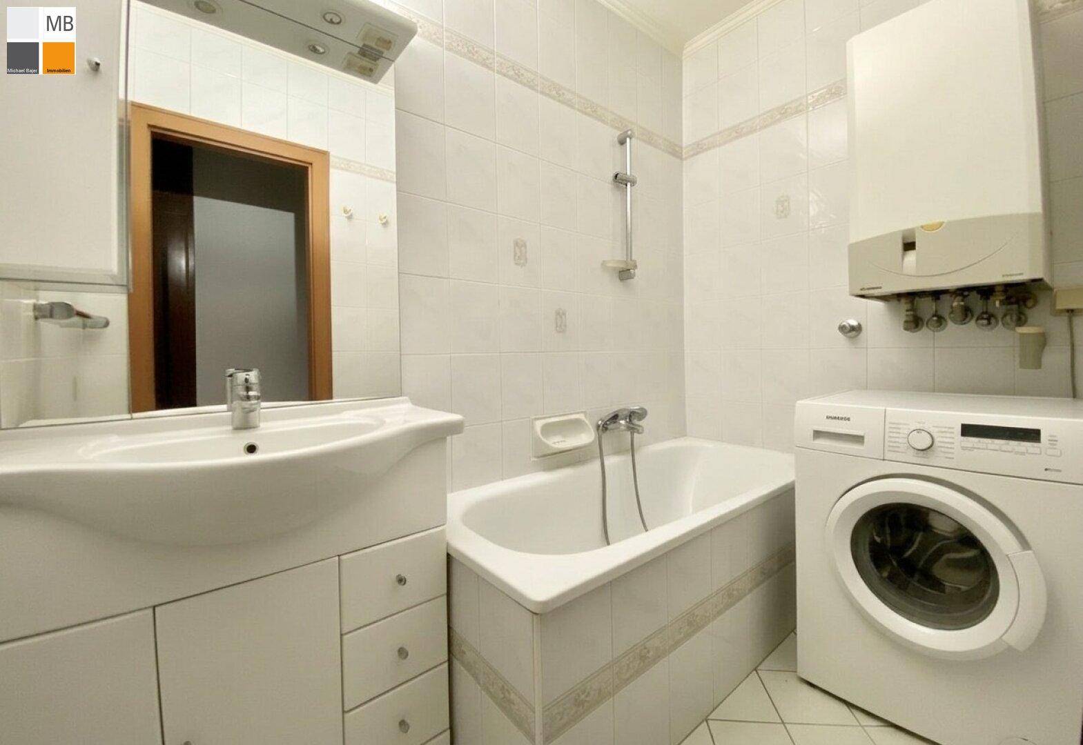 Klassisches Badezimmer mit Badewanne, Waschbecken und Waschmaschine, hell gefliest.