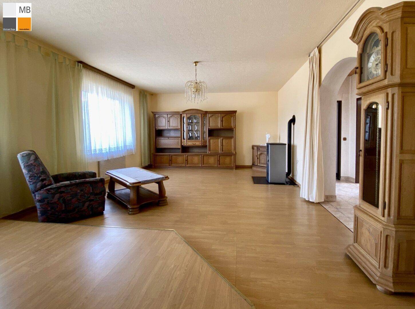Helles Wohnzimmer mit großem Fenster, Holzofen und traditioneller Einrichtung.