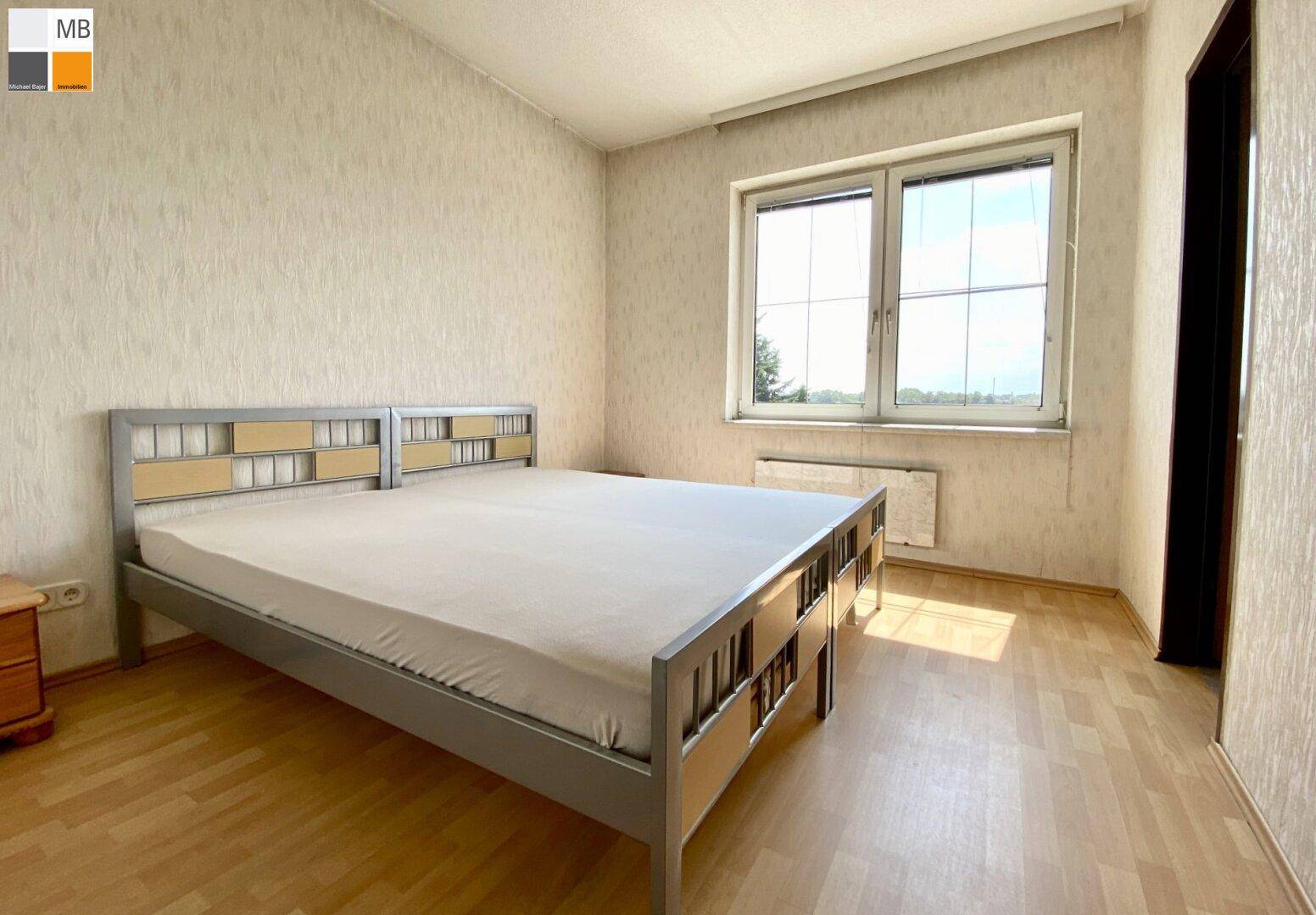 Schlafzimmer mit Doppelbett, hellem Laminatboden und Fenster mit weitem Ausblick.