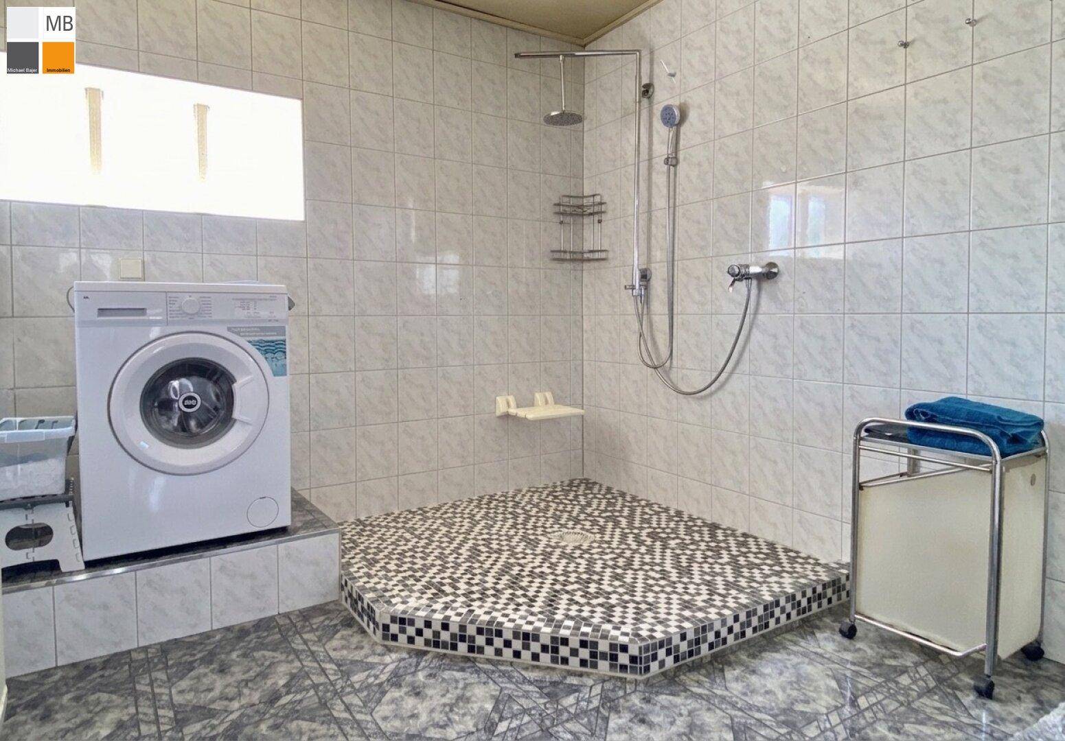 Badezimmer mit Duschbereich, Waschmaschine und hellen Fliesen an Wänden und Boden.