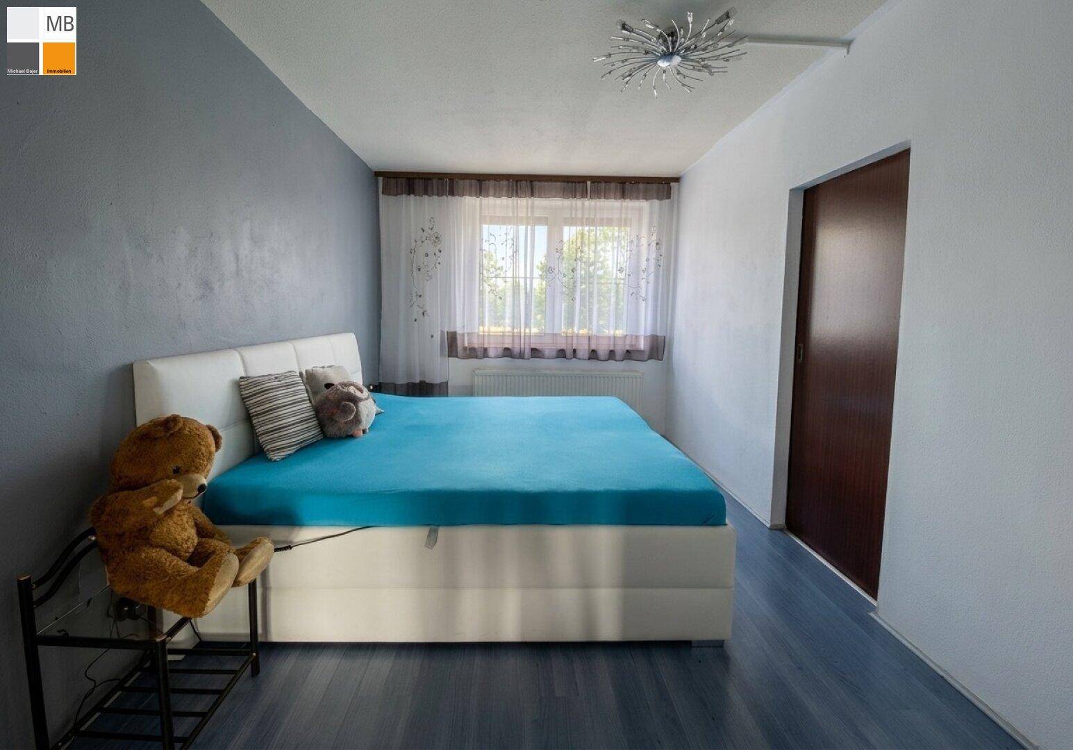 Schlafzimmer mit Doppelbett, blauer Boden und Fenster mit Vorhängen.