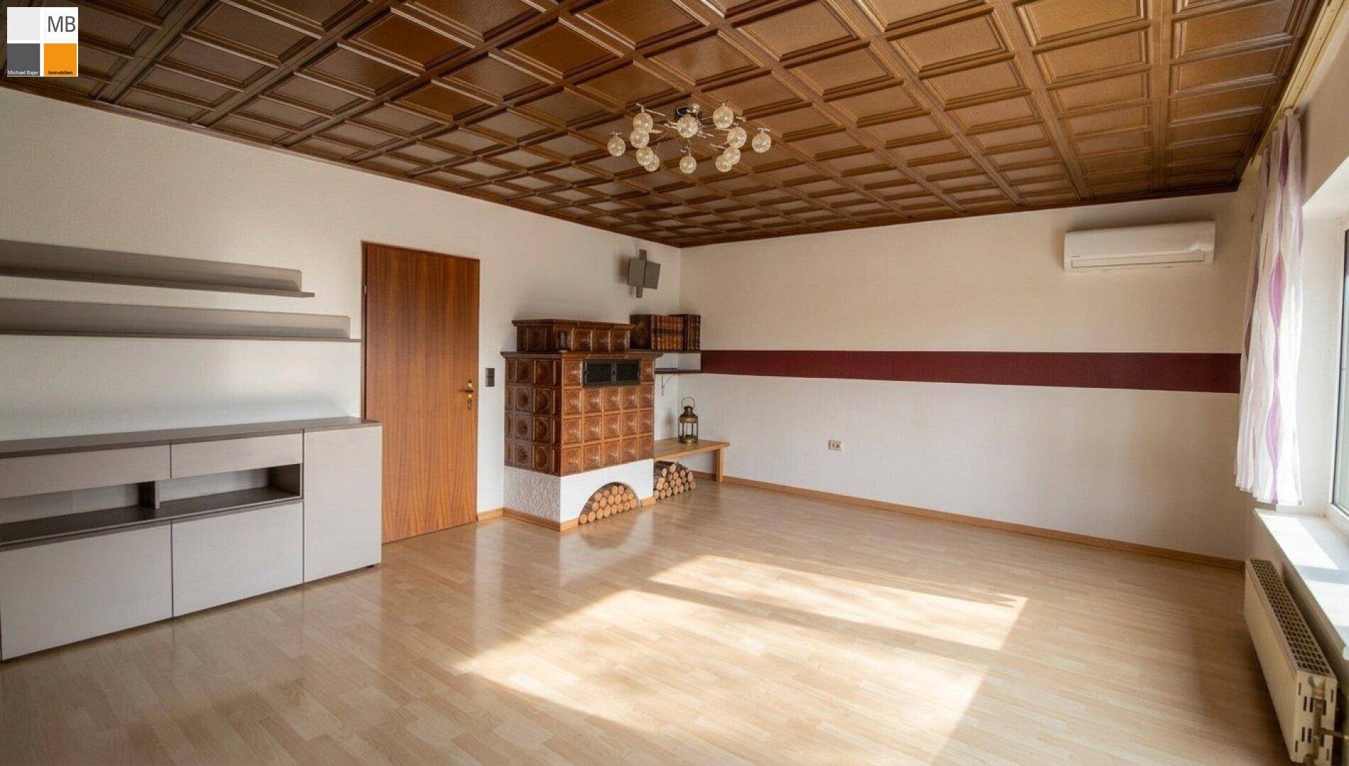 Geräumiges Wohnzimmer mit Kachelofen, Holzkassettendecke und hellem Parkettboden.