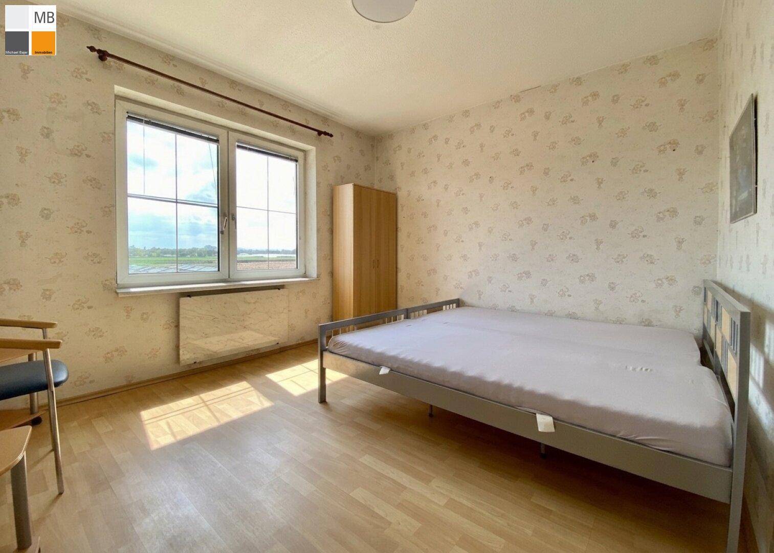 Helles Schlafzimmer mit Laminatboden, Kleiderschrank und Fenster mit Ausblick.