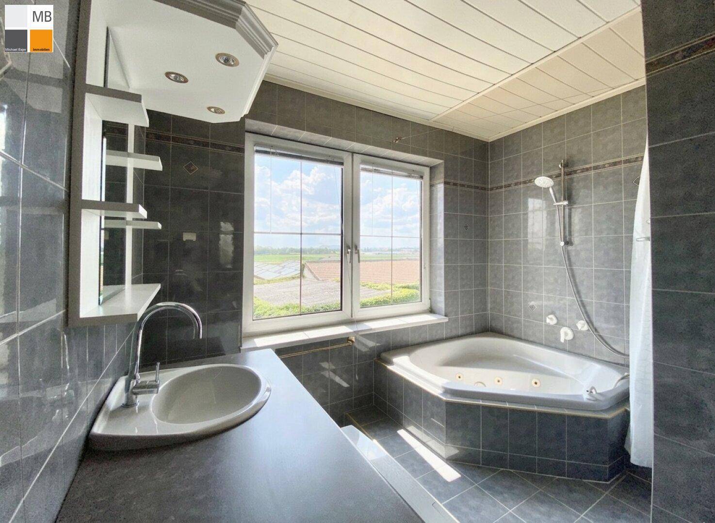 Badezimmer mit dunklen Fliesen, Eck-Whirlpool und großem Fenster mit Ausblick.