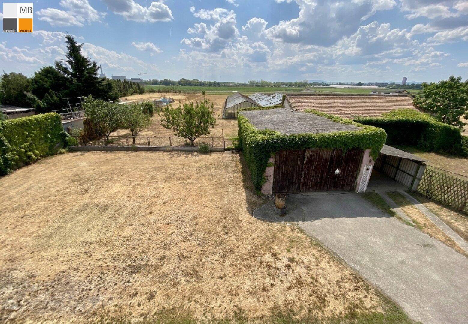 Blick von oben auf den Gartenbereich mit Garage, trockenem Rasen und Gewächshäusern.