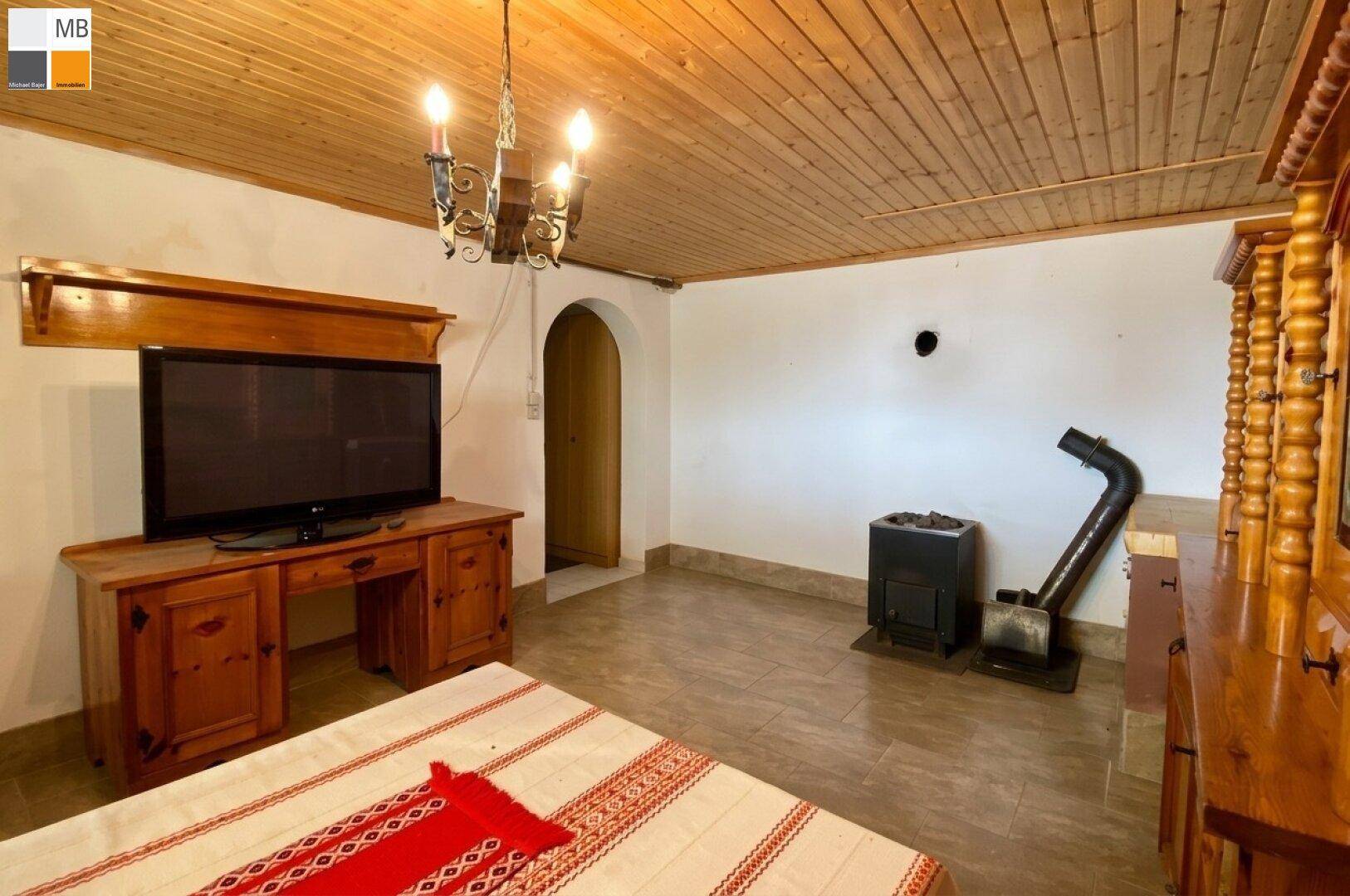 Gemütlicher Raum mit Holzbalkendecke, traditionellem Ofen und rustikalen Holzmöbeln.