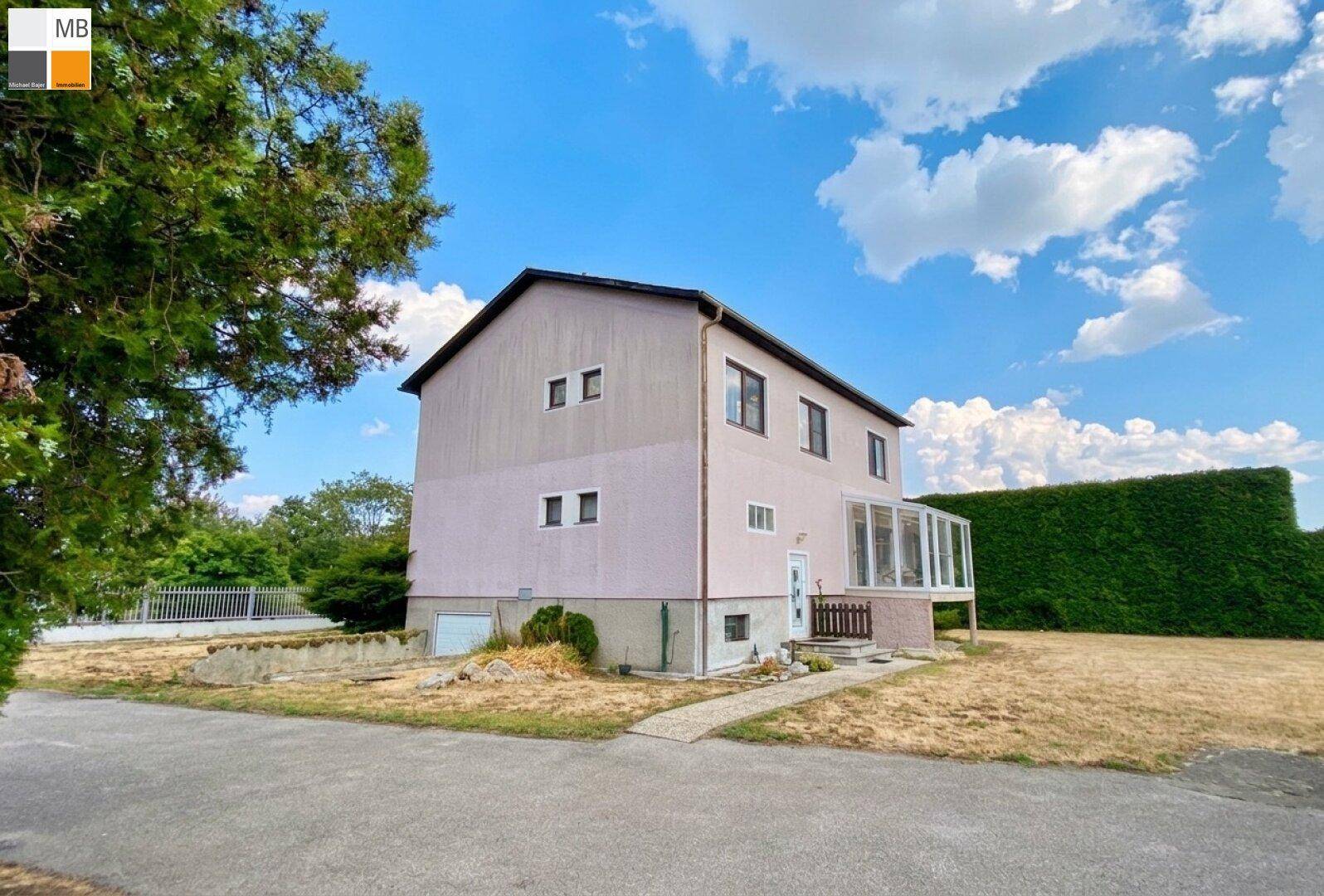 Einfamilienhaus mit rosa Fassade, Wintergarten und großem Gartenbereich unter blauem Himmel.