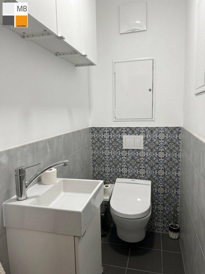 Modernes Gäste-WC mit Wand-WC, Waschbecken und dekorativen Fliesen.