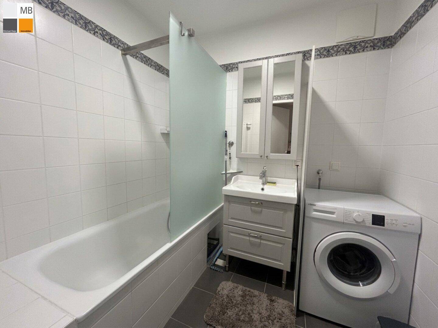 Badezimmer mit Badewanne, Waschmaschine, Waschbecken und Spiegelschrank.