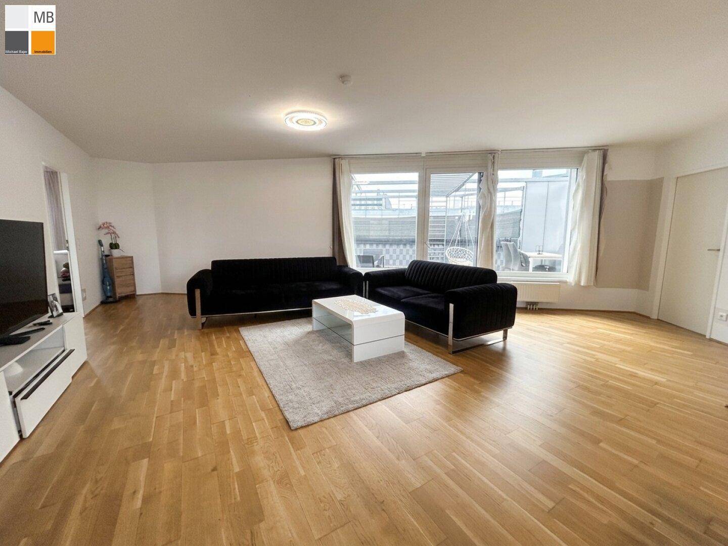 Helles Wohnzimmer mit Parkettboden, zwei Sofas und Zugang zur Dachterrasse.