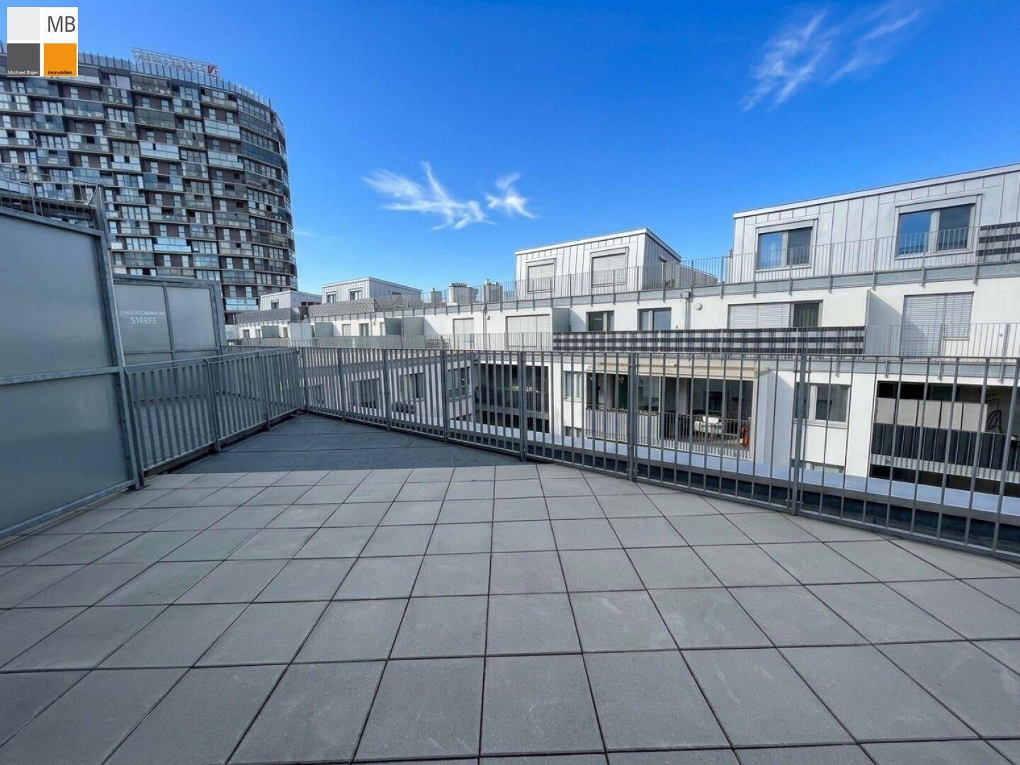 Große geflieste Terrasse mit Metallgeländer und Blick auf moderne Gebäude.