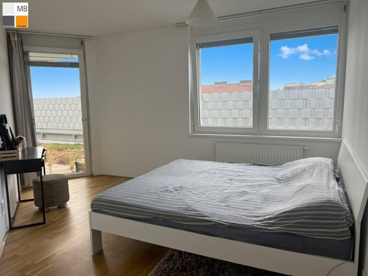 Helles Schlafzimmer mit Parkettboden, großem Fenster und Zugang zu einem Außenbereich.