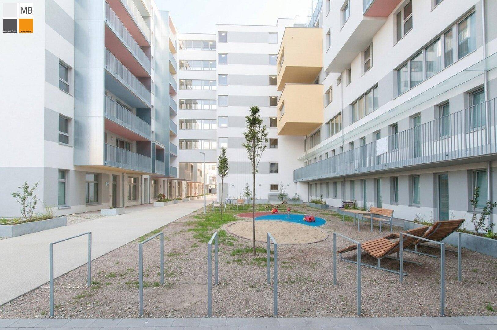 Innenhof eines modernen Wohnkomplexes mit Spielplatz und Sitzgelegenheiten.