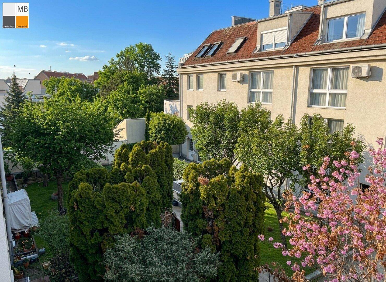 Blick auf den grünen Innenhof mit Bäumen und blühenden Sträuchern, umgeben von Wohngebäuden.