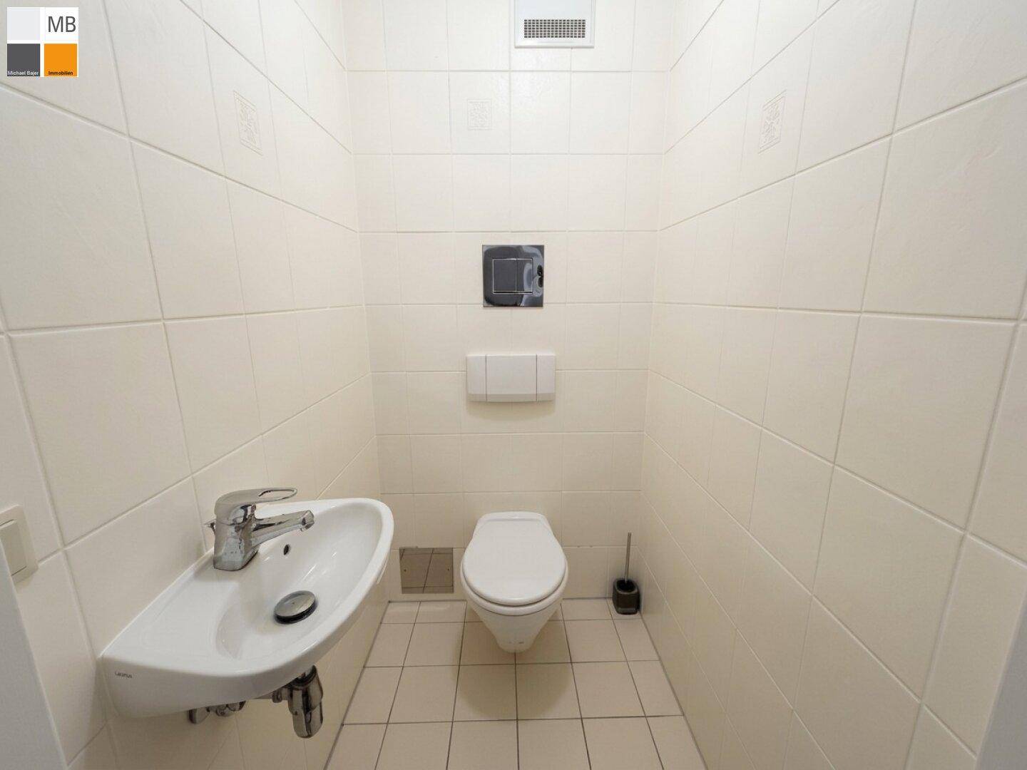 Modernes Gäste-WC mit hellen Fliesen, wandhängendem WC und kleinem Waschbecken.