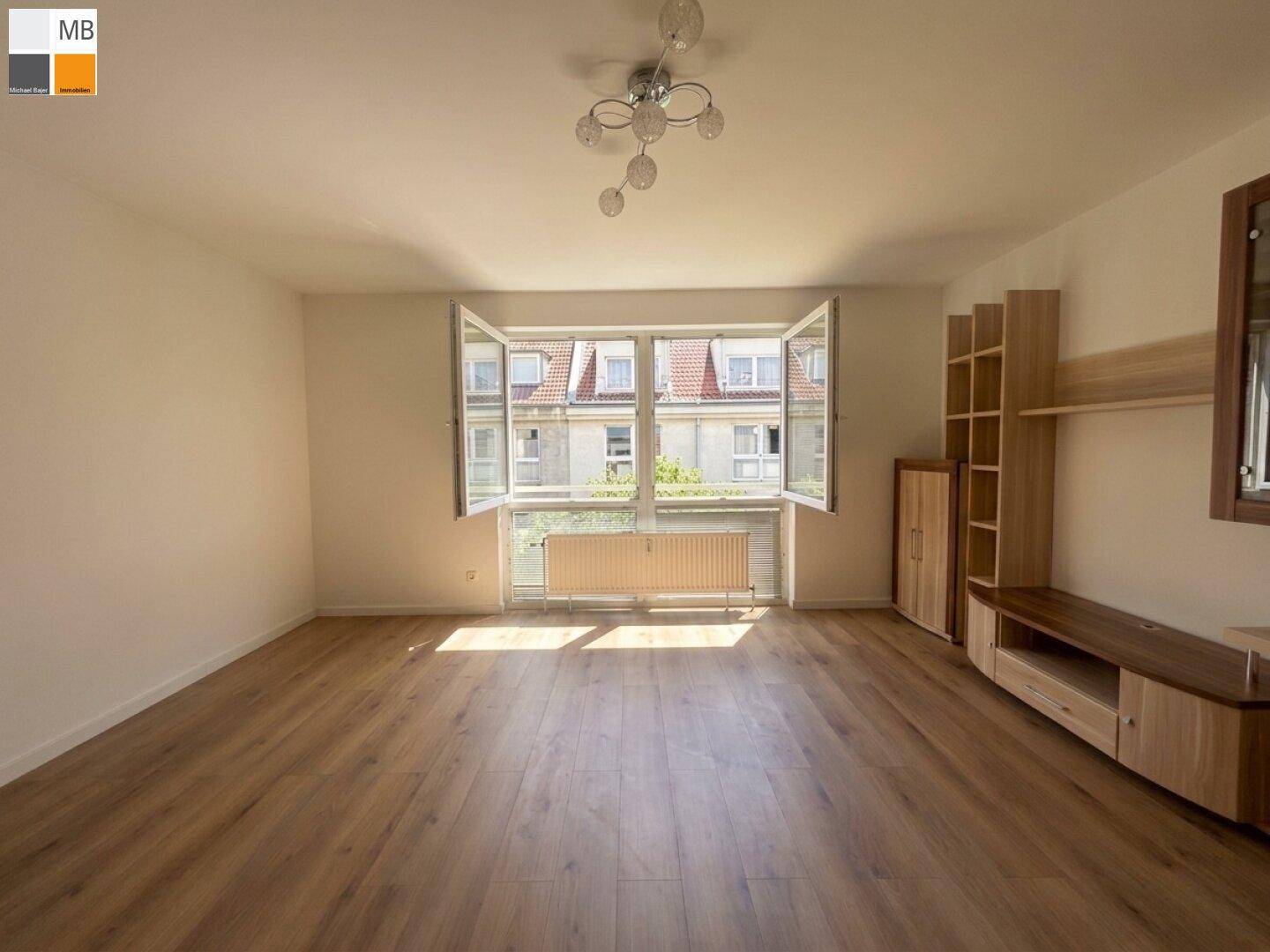 Geräumiges Wohnzimmer mit Laminatboden und großem Fenster, das viel Tageslicht hereinlässt.