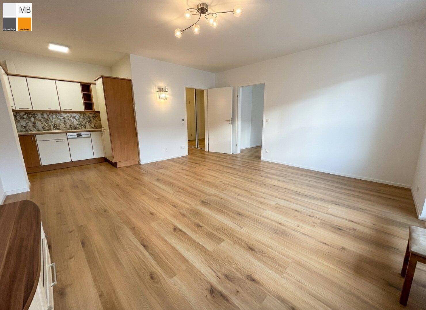 Heller offener Wohnbereich mit Laminatboden und integrierter Küchenzeile, ideal für modernes Wohnen.
