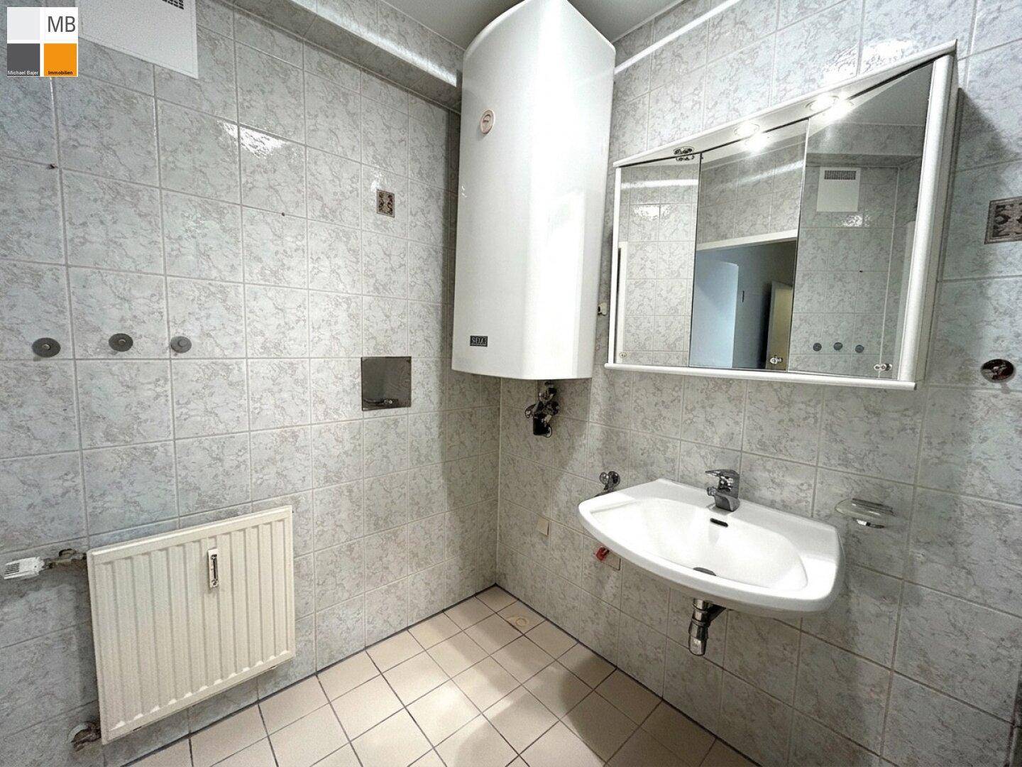 Badezimmer mit hellen Fliesen, Waschbecken, Spiegelschrank und Heizkörper, funktional und sauber.