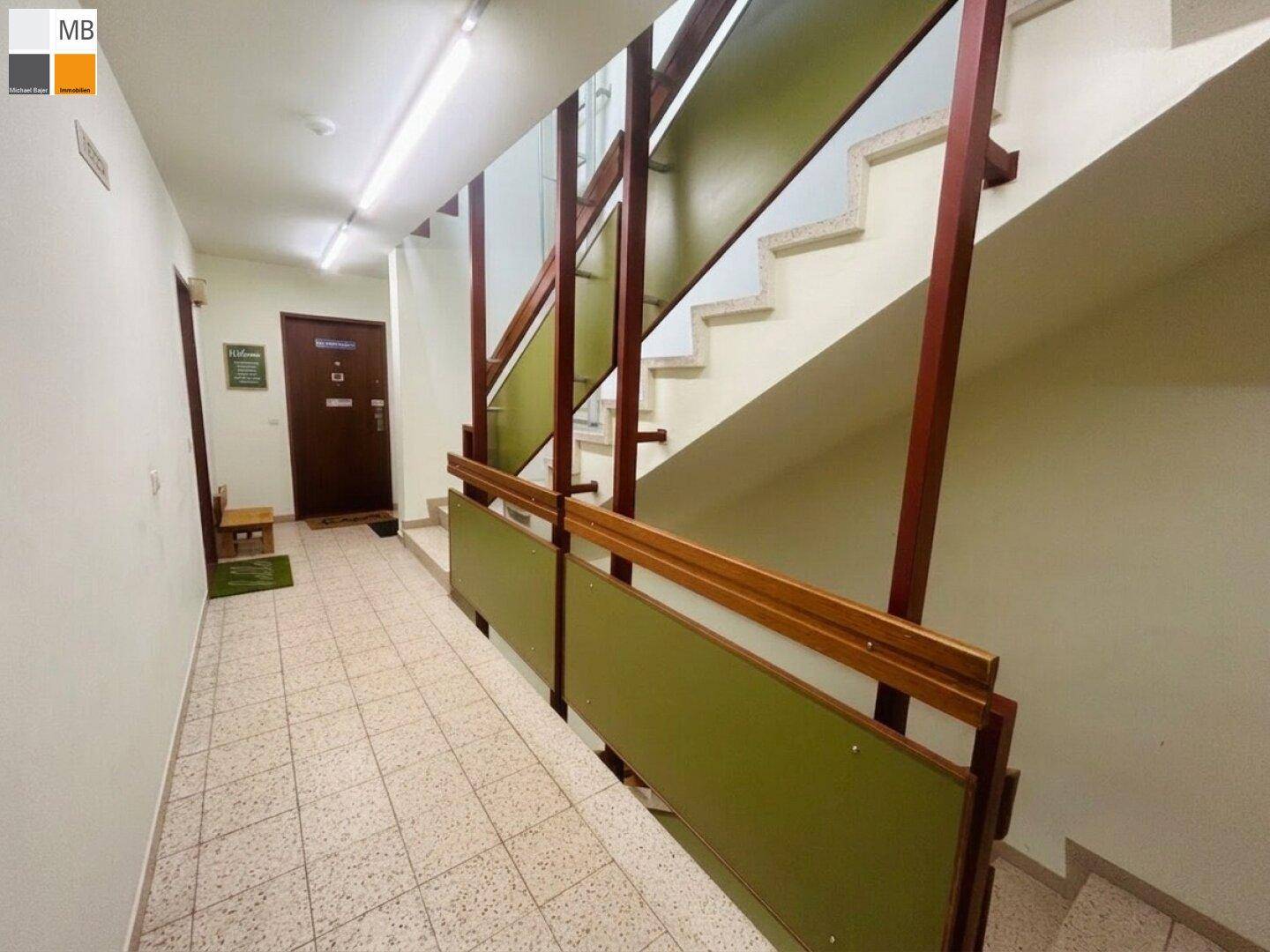 Gemeinschaftliches Treppenhaus mit gefliestem Boden und robustem Geländer in Grün- und Brauntönen.