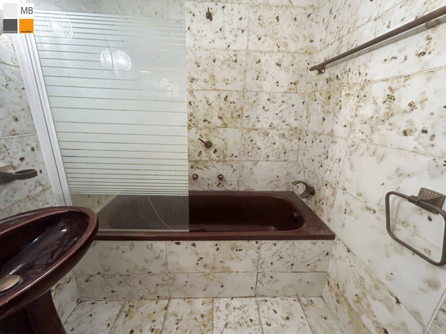Badezimmer mit gemusterten Fliesen, einer dunklen Badewanne und einer Duschabtrennung.