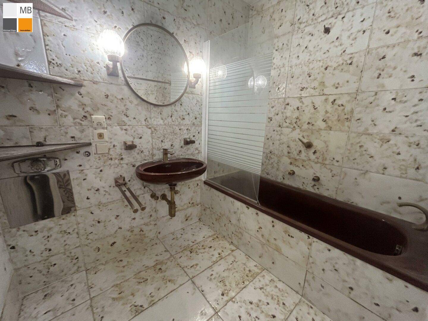 Badezimmer mit gemusterten Fliesen, Waschbecken, Spiegel und Beleuchtung über der Badewanne.