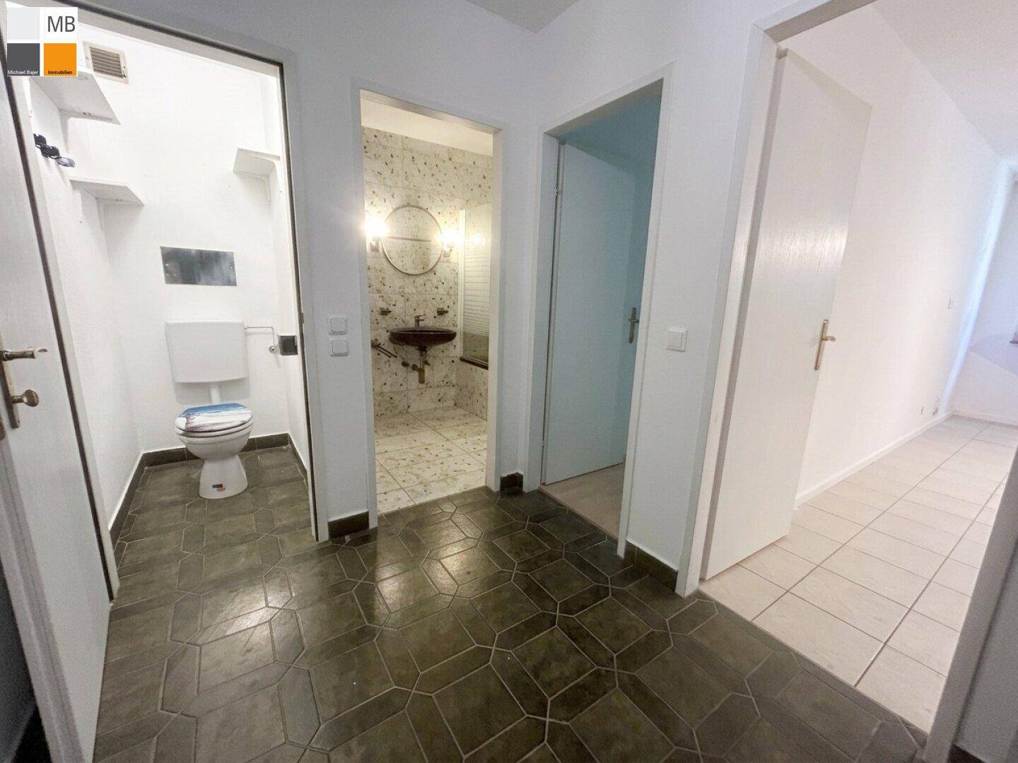 Flur mit dunklen, gemusterten Bodenfliesen und Zugängen zu Badezimmer und separatem WC.