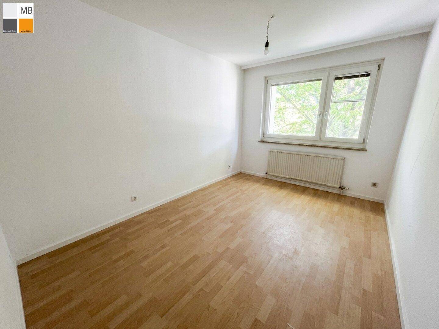 Leeres Zimmer mit hellem Parkettboden, weißen Wänden und einem großen Fenster für viel Licht.