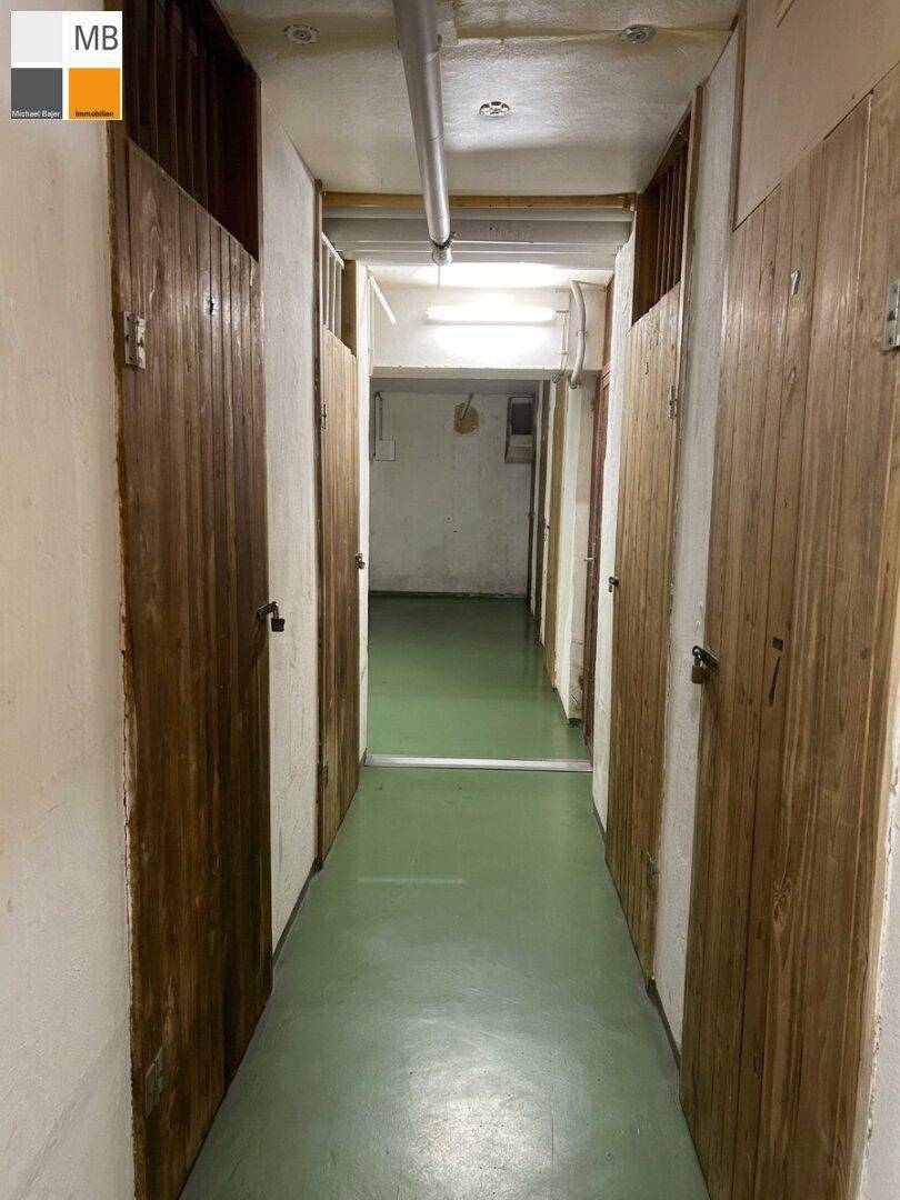 Langer Kellergang mit Holzverschlägen auf beiden Seiten, ideal für zusätzlichen Stauraum.