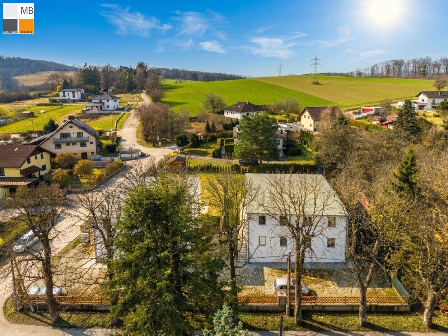 Weitläufige Luftaufnahme der ländlichen Umgebung mit mehreren Wohnhäusern und grünen Hügeln.