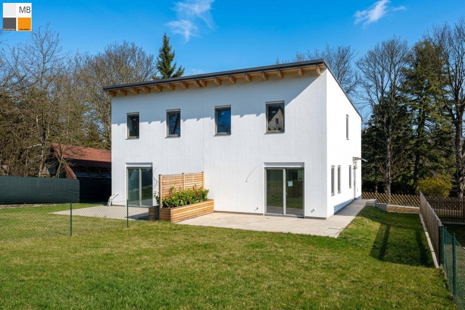 Rückseite des modernen Einfamilienhauses mit großem Garten und Terrasse unter blauem Himmel.