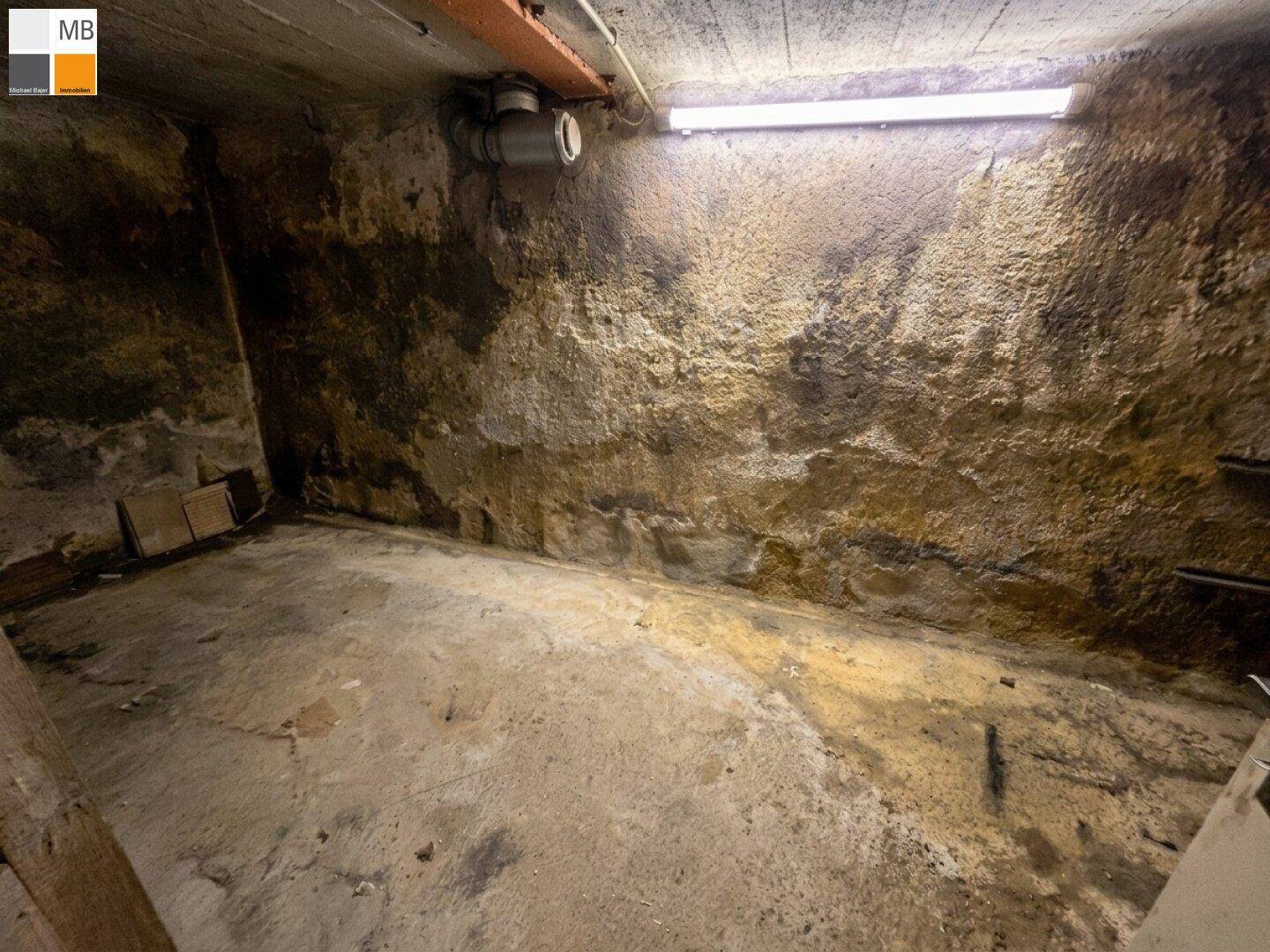 Unfertiger Kellerraum mit rauen Wänden, Betonboden und sichtbaren Leitungen.