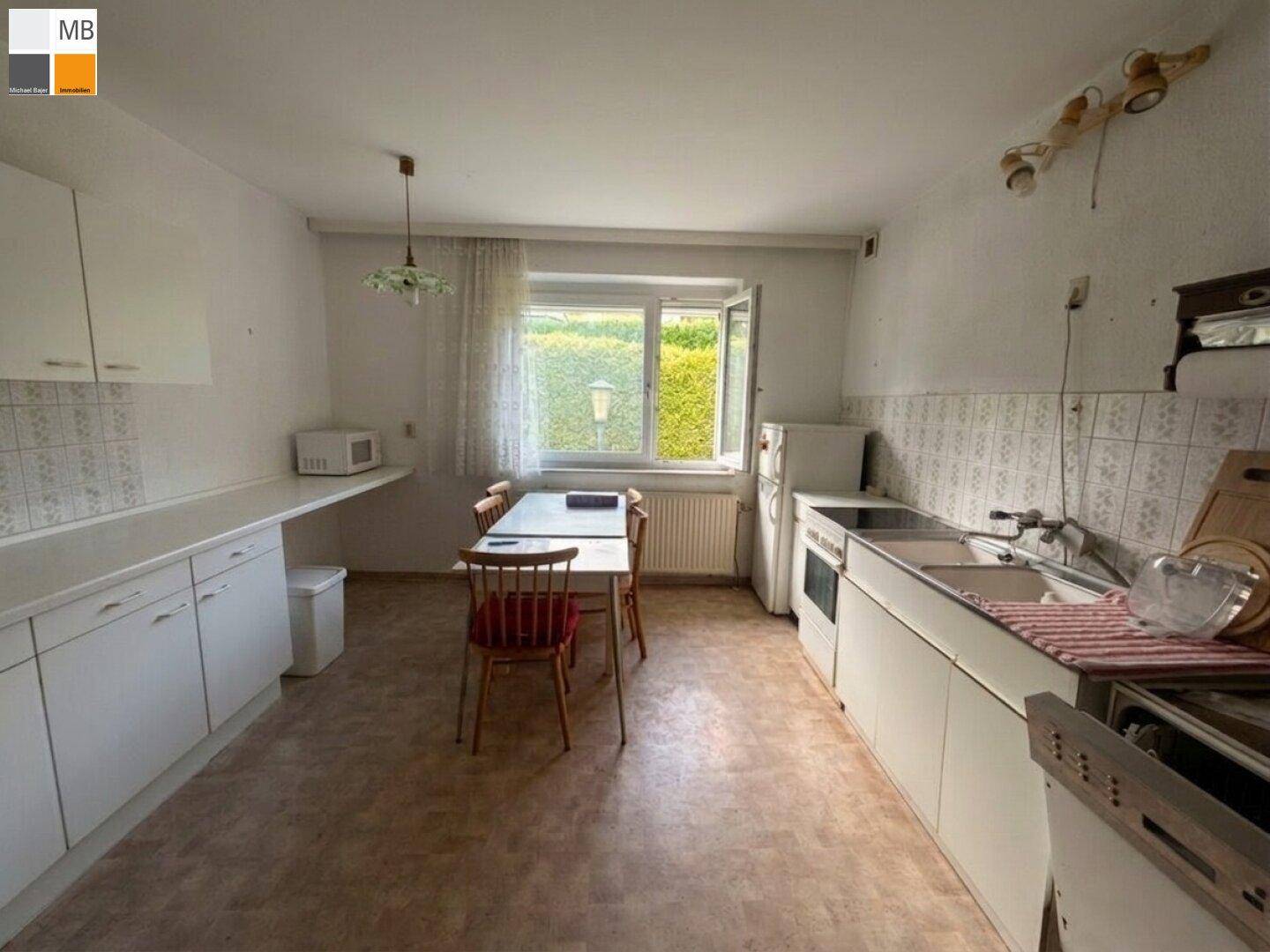 Funktionale Einbauküche mit Essbereich, Fenster und Blick auf eine grüne Hecke.