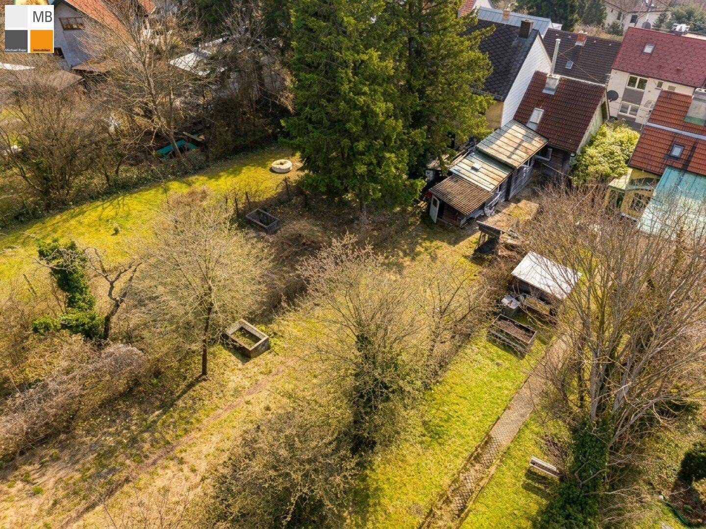 Luftaufnahme eines grünen Gartengrundstücks mit einem kleinen Schuppen und angrenzenden Wohnhäusern.