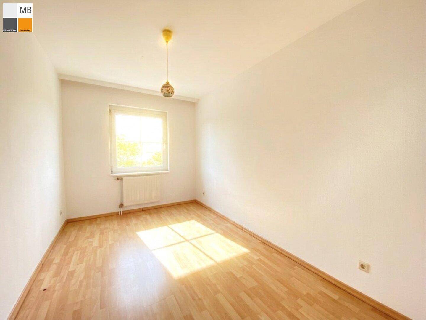 Helles Schlafzimmer mit Laminatboden und einem Fenster, das viel Tageslicht hereinlässt.