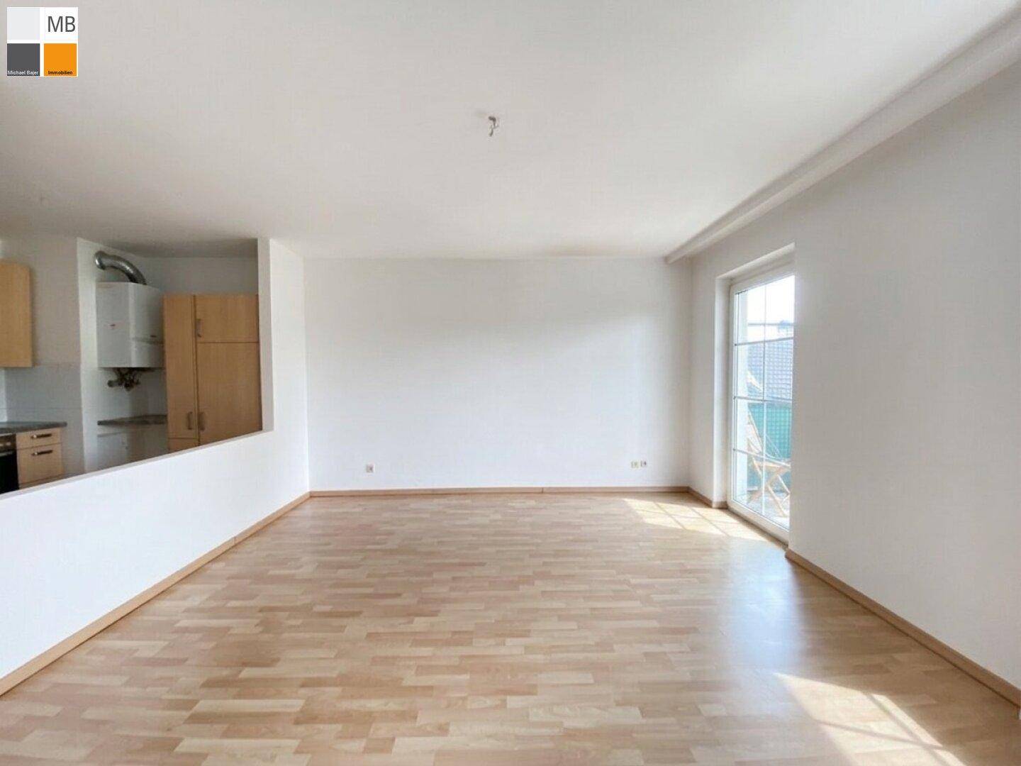 Heller Wohnbereich mit Laminatboden und Blick auf die teilweise offene Küche mit Holzschränken.