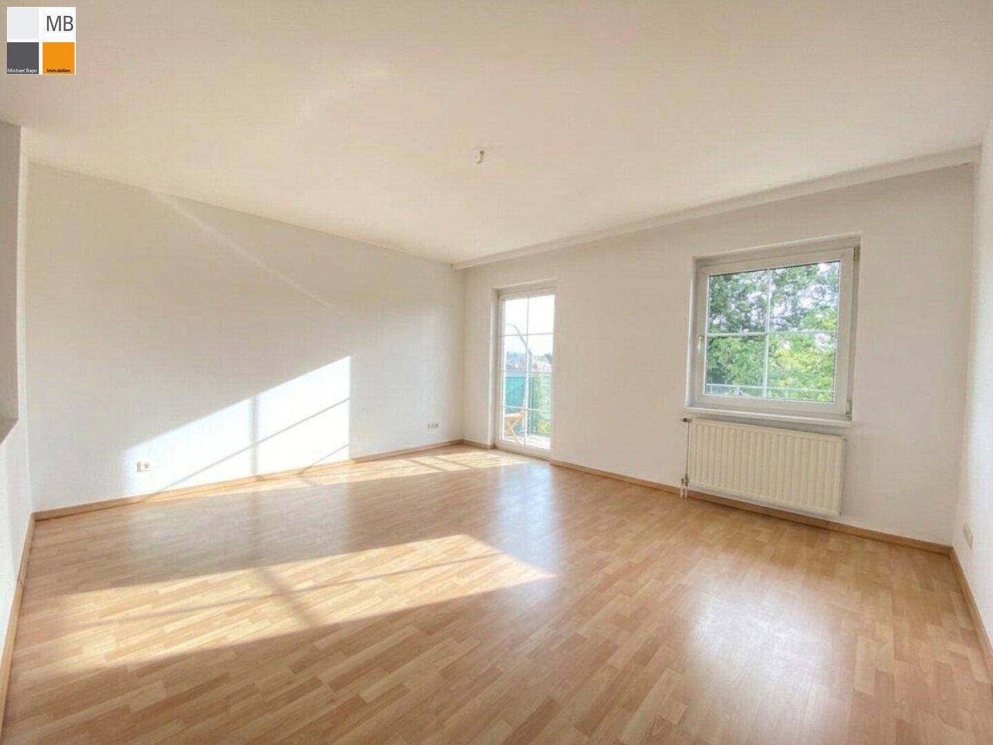 Geräumiges Wohnzimmer mit hellem Laminatboden, großen Fenstern und Zugang zu einem Außenbereich.