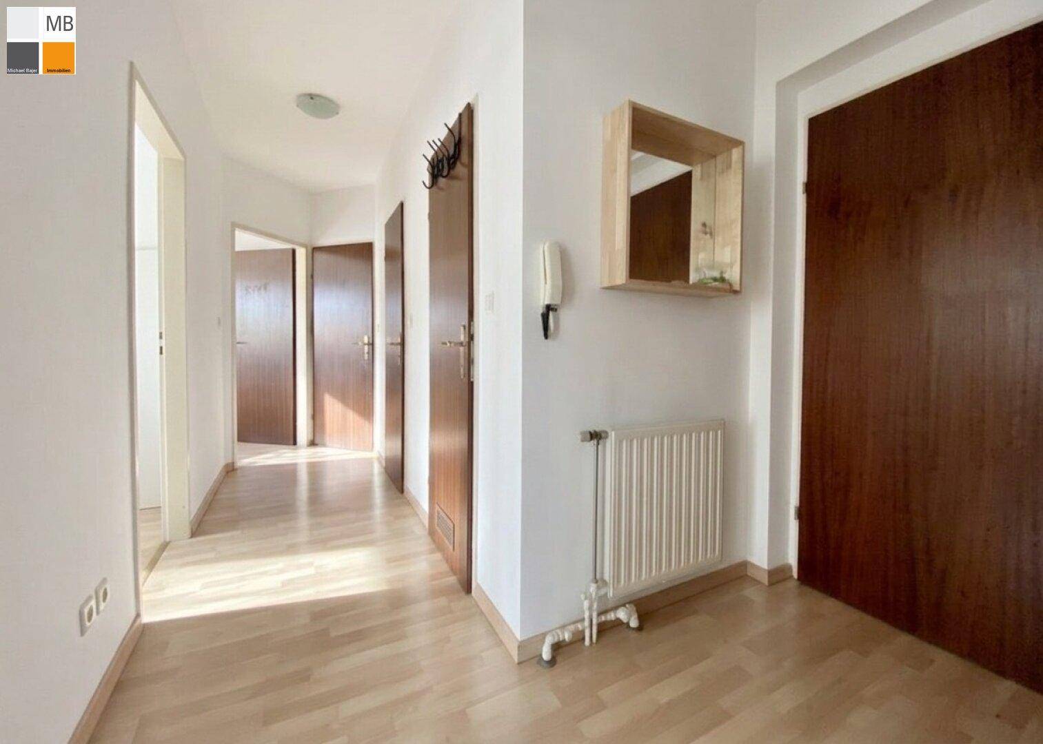 Heller Flur mit Laminatboden, mehreren Türen und einem Heizkörper an der Wand.