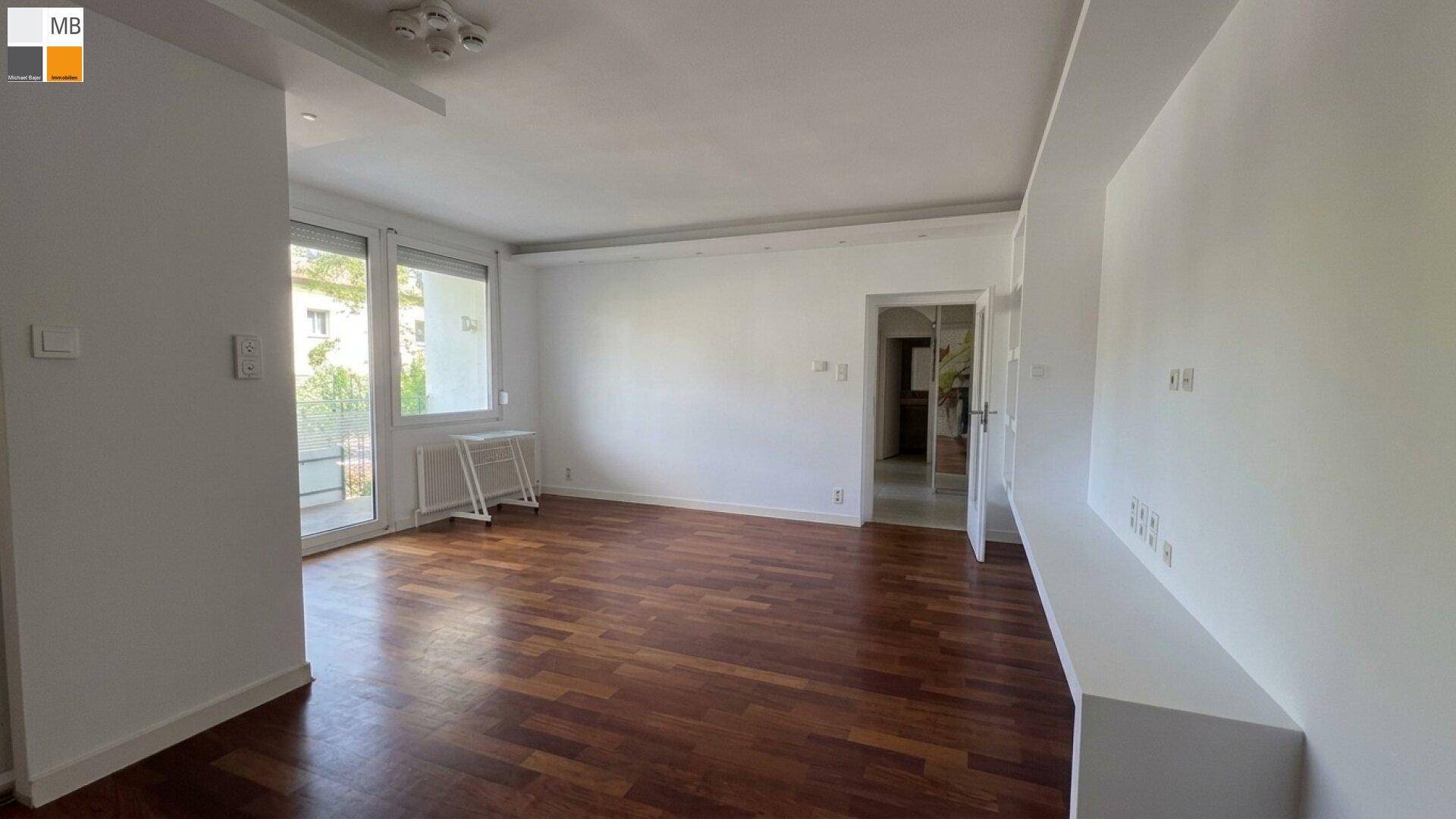 Helles Wohnzimmer mit Holzboden und Zugang zu einem weiteren Raum.