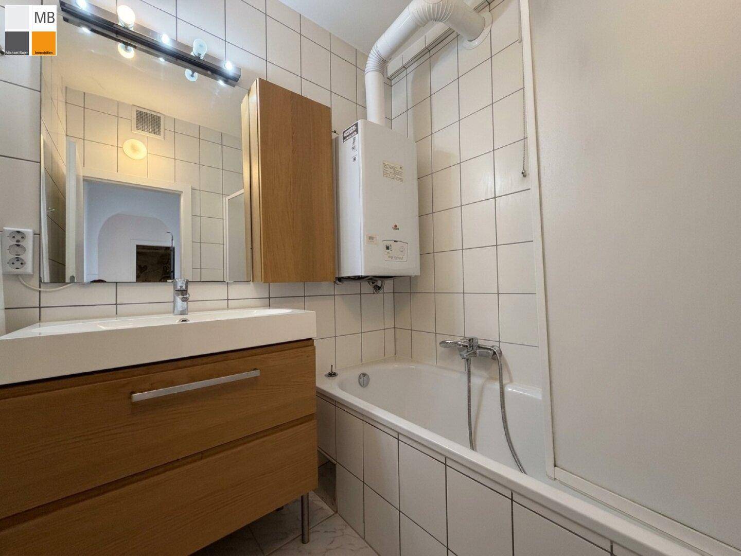 Badezimmer mit Waschtisch, Spiegel und Badewanne mit Duschfunktion.