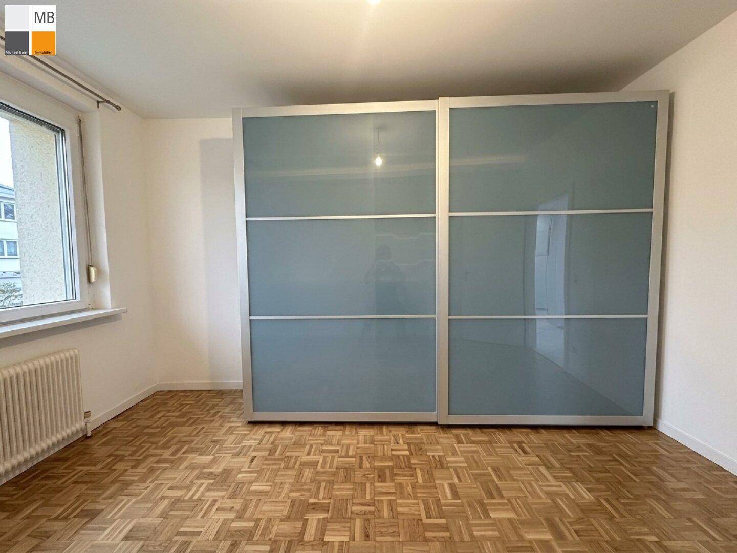 Schlafzimmer mit Parkettboden und großem Schiebeschrank mit Spiegelfronten.