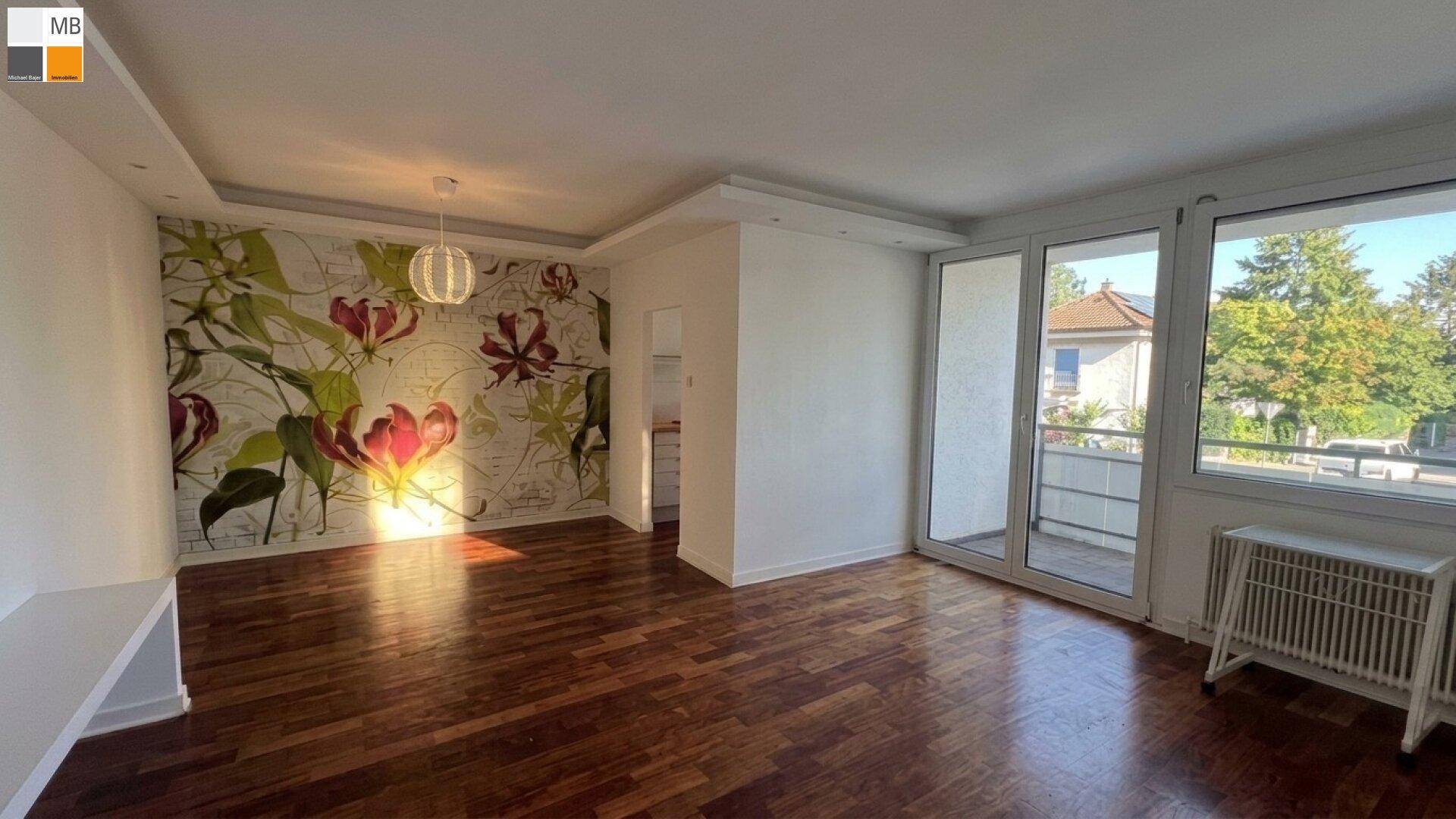Wohnzimmer mit Holzboden, floraler Tapete und Zugang zum Balkon.